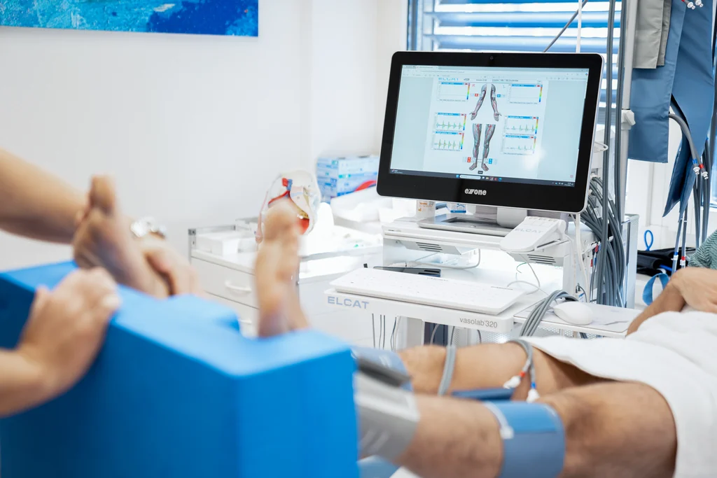 Messung des Knöchel-Arm-Index mit Blutdruckmanschetten an Beinen und Arm in der Hausarztpraxis Wohlen
